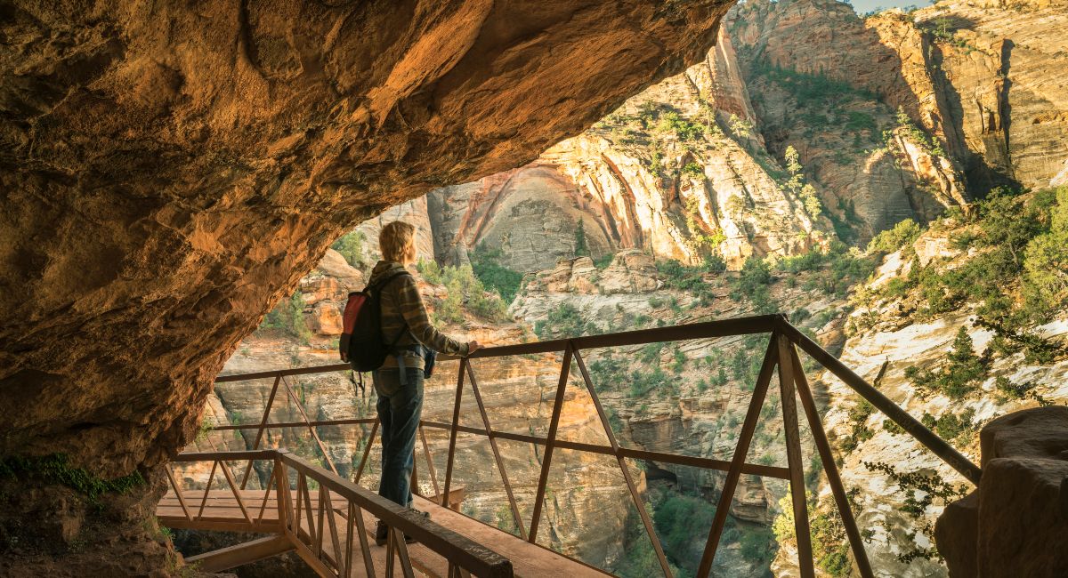 A tourist with a backpack observing the breathtaking sunrise from an overlook in Zion Canyon, showcasing the majestic beauty of the sandstone cliffs and expansive views of the national park