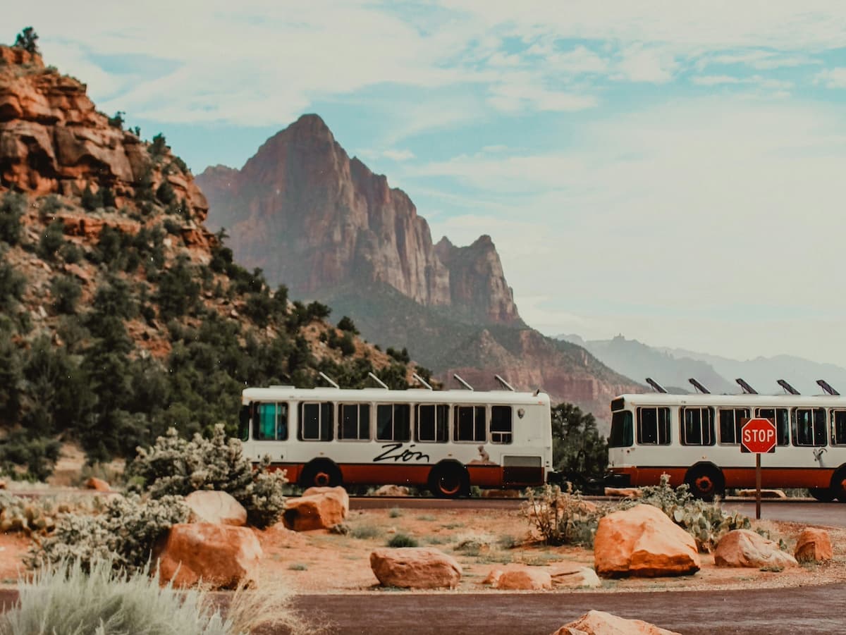 View of the red and white Zion Canyon Shuttle with large red rock mountain in background