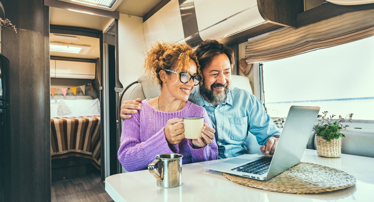 Modern adult couple in front of a laptop inside their motorhome, smiling as they  calculate the cost of their RV insurance