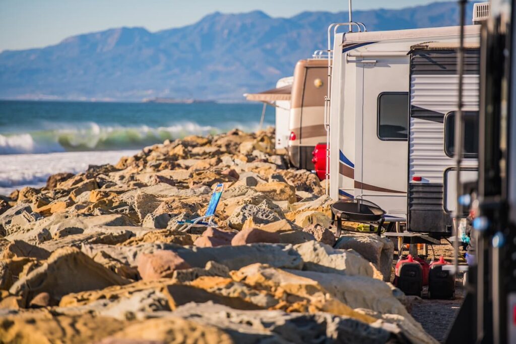 A line of RV motorhomes lined up next to a rocky beach in California