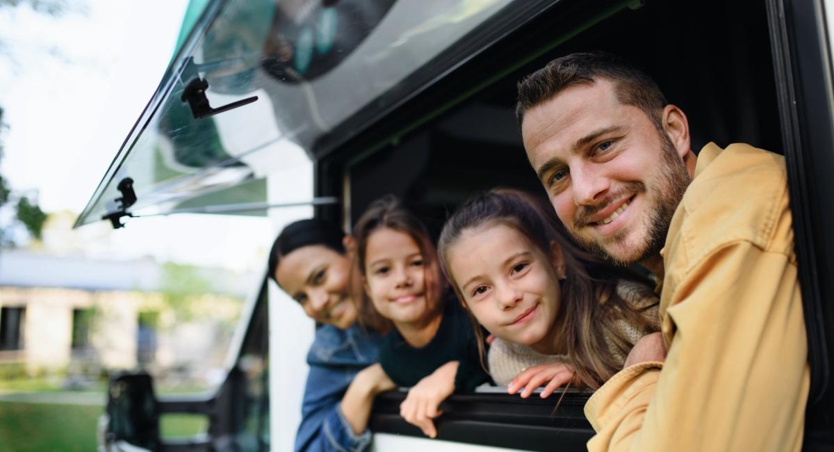 Excited family of four sitting together in an RV smiling and looking out the open window ready for a road trip adventure