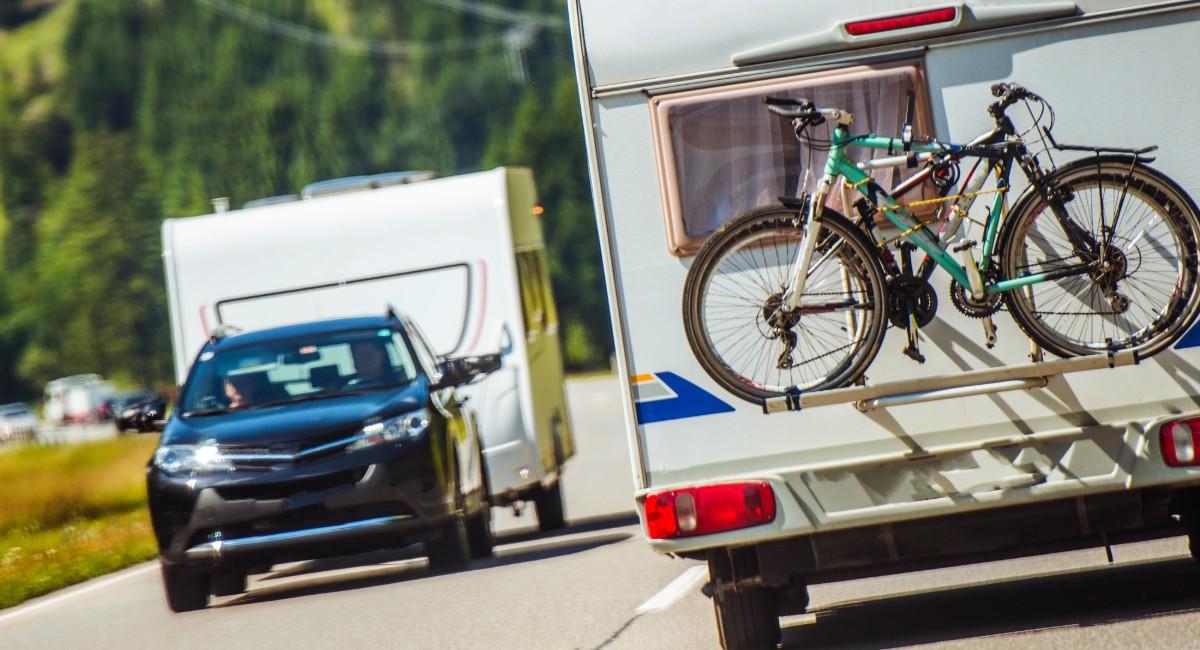 SUV towing white travel trailer on scenic road with mountain bikes mounted on rear cargo carrier for family RV camping trip