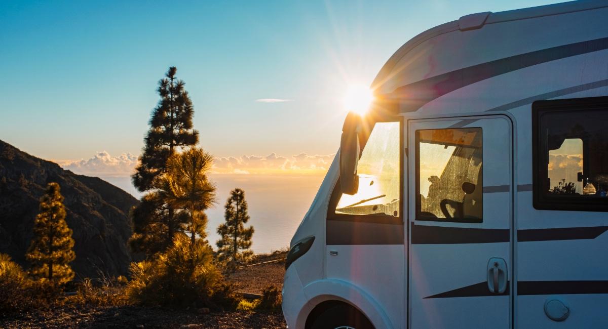 White Class C motorhome parked in scenic mountain location during golden sunset with dramatic landscape background