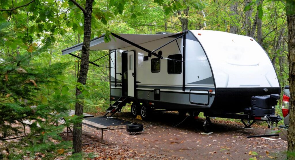 Lightweight travel trailer set up at wooded campsite with awning extended, demonstrating easy setup for family camping adventures under 3000 lbs