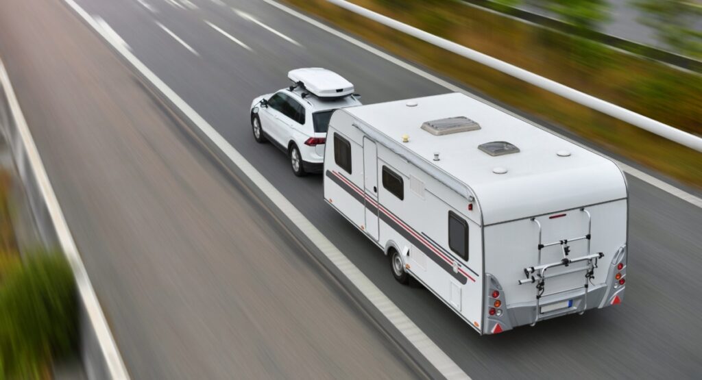 White SUV towing lightweight travel trailer under 3000 lbs on highway, demonstrating easy towing capability for weekend RV adventures