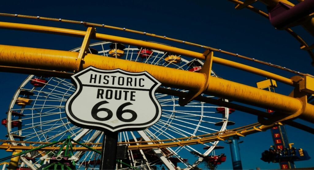 A close-up street sign near a Ferris wheel in Los Angeles Route 66