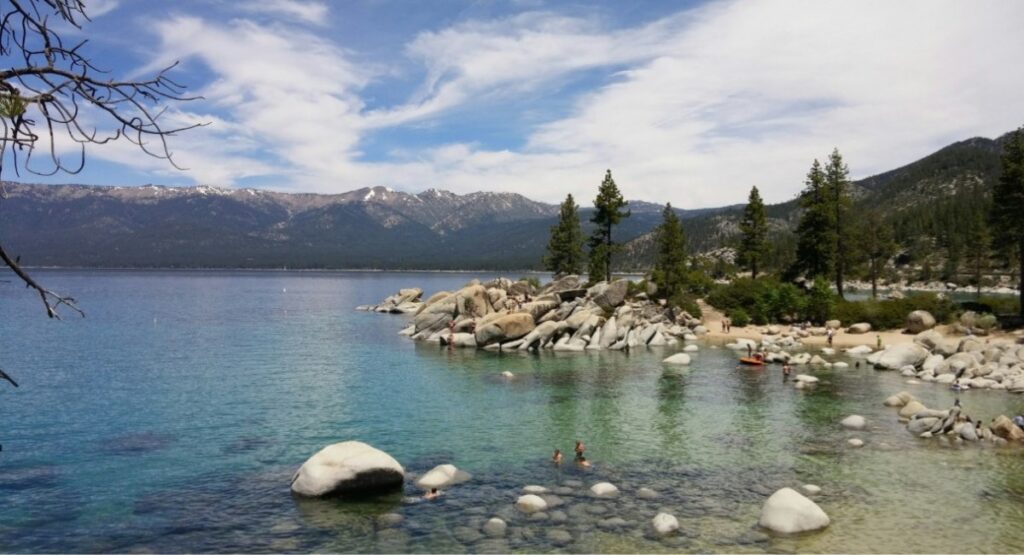 Swimmers enjoying the clear turquoise waters of Lake Tahoe, surrounded by granite boulders and pine trees